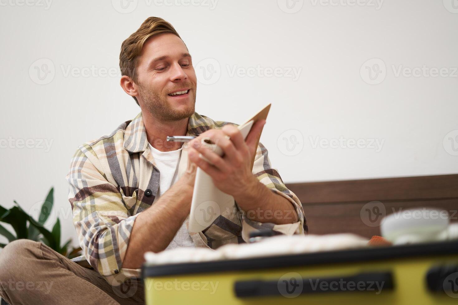 Portrait of thoughtful young man, tourist going on vacation, going through holiday check-list, writing down what he wants to take on travelling photo