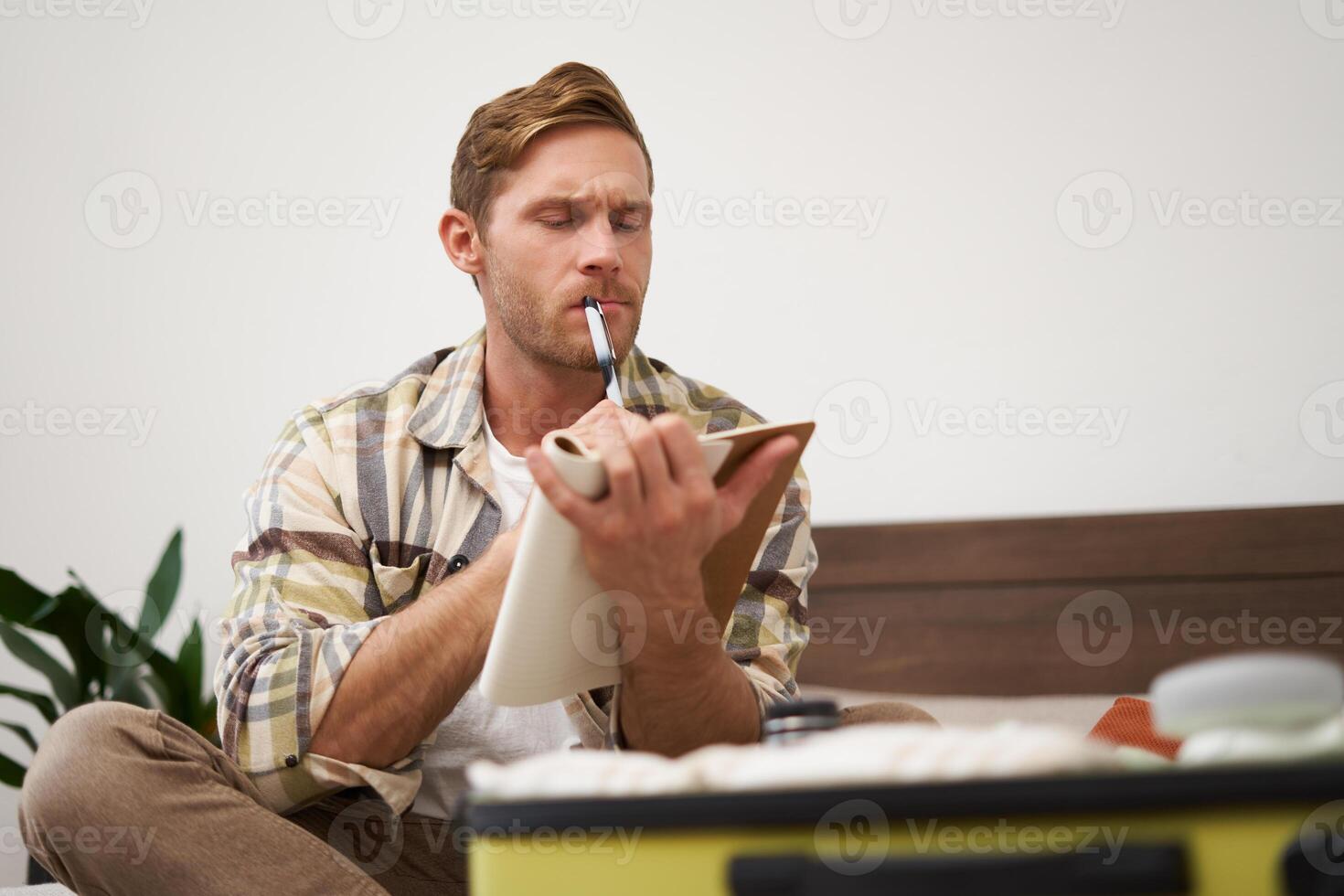 Portrait of thoughtful young man, tourist going on vacation, going through holiday check-list, writing down what he wants to take on travelling photo