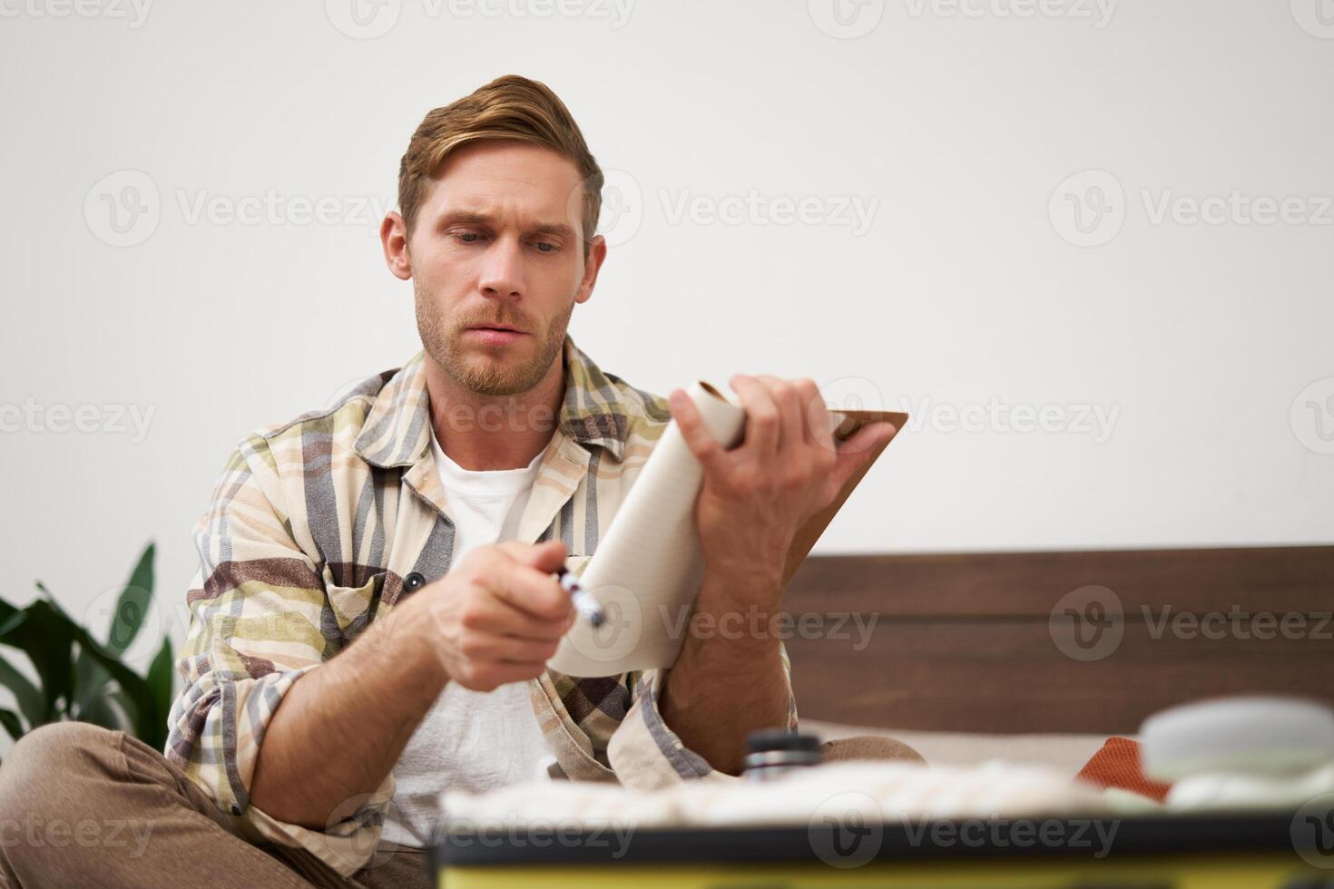 Portrait of thoughtful young man, tourist going on vacation, going through holiday check-list, writing down what he wants to take on travelling photo
