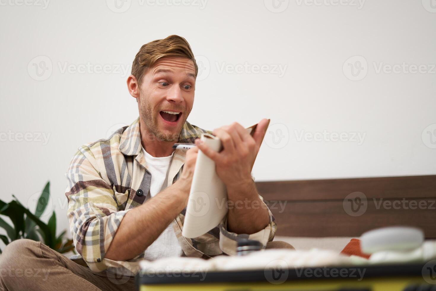Portrait of charismatic, handsome man, tourist looking at notebook, getting ready for journey, packing suitcase, checking list of items on journal photo