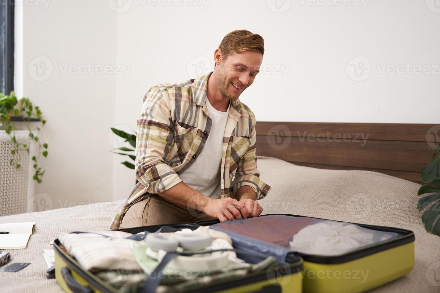 Portrait of young man, closing suitcase, packing for holiday, preparing to go on vacation or business trip, getting luggage ready for a trip photo