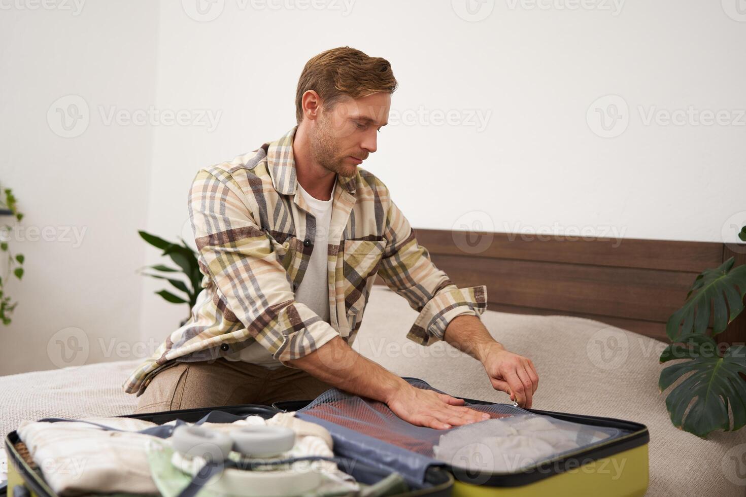 Portrait of young man, closing suitcase, packing for holiday, preparing to go on vacation or business trip, getting luggage ready for a trip photo