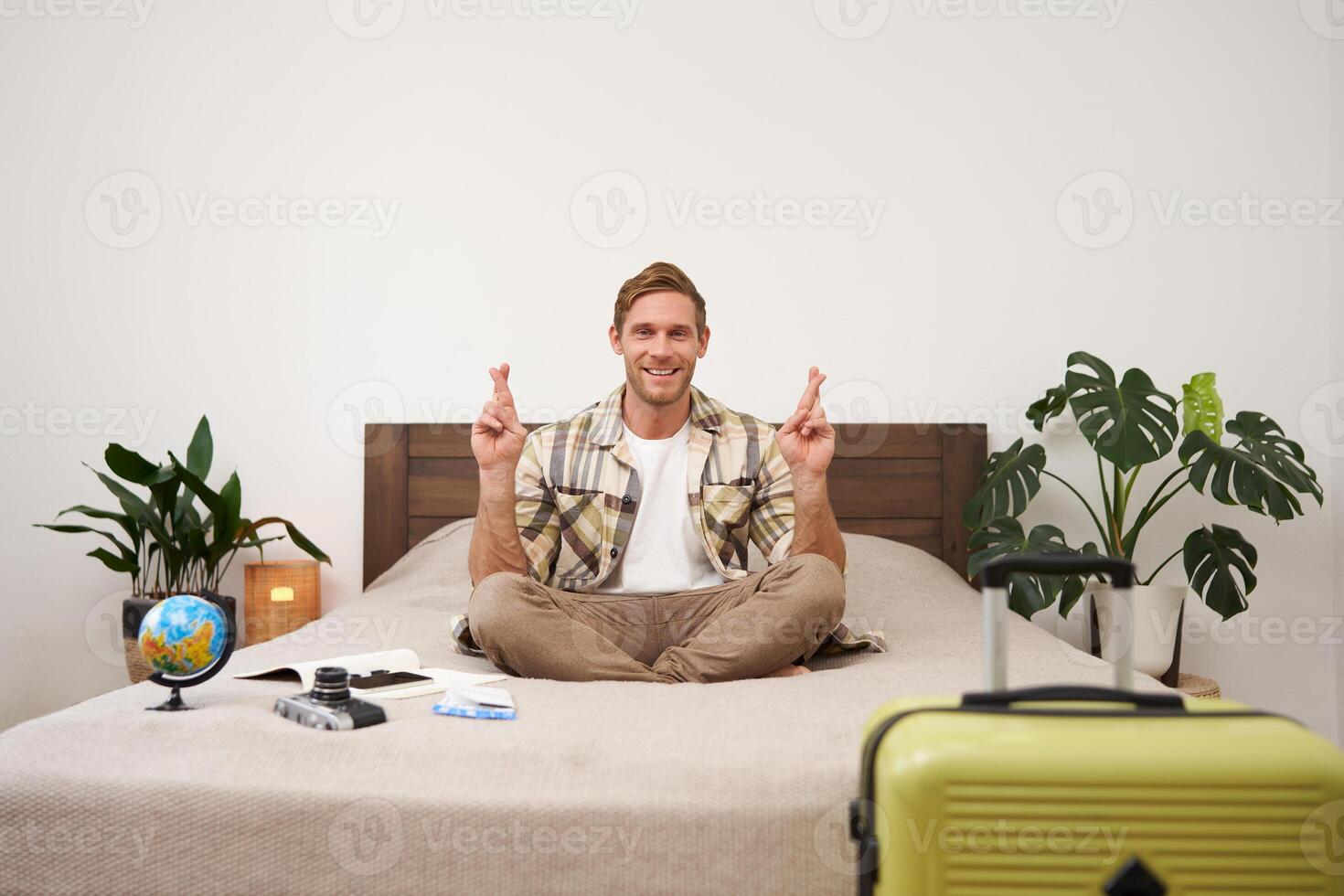 Portrait of young man meditating on a bed after packing suitcase for summer holiday, sitting with crossed legs in zen, nirvana pose, relaxing, hoping for something photo