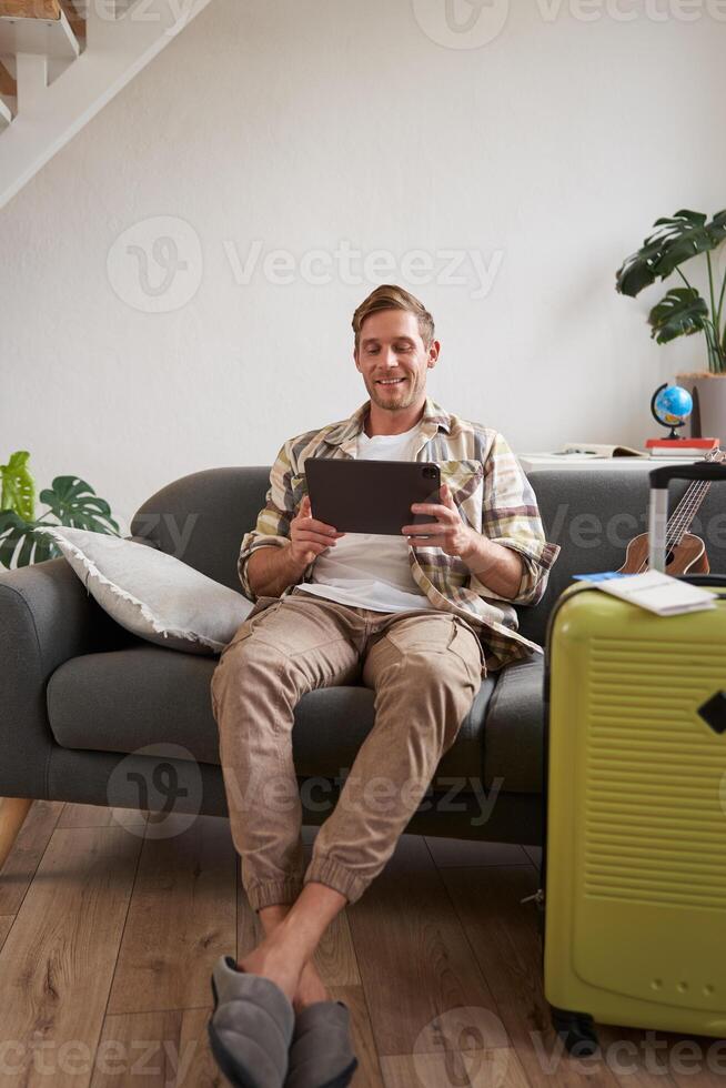 Vertical shot of man, tourist with suitcase, looking at digital tablet, reading about travel destination, booking hotel on gadget photo