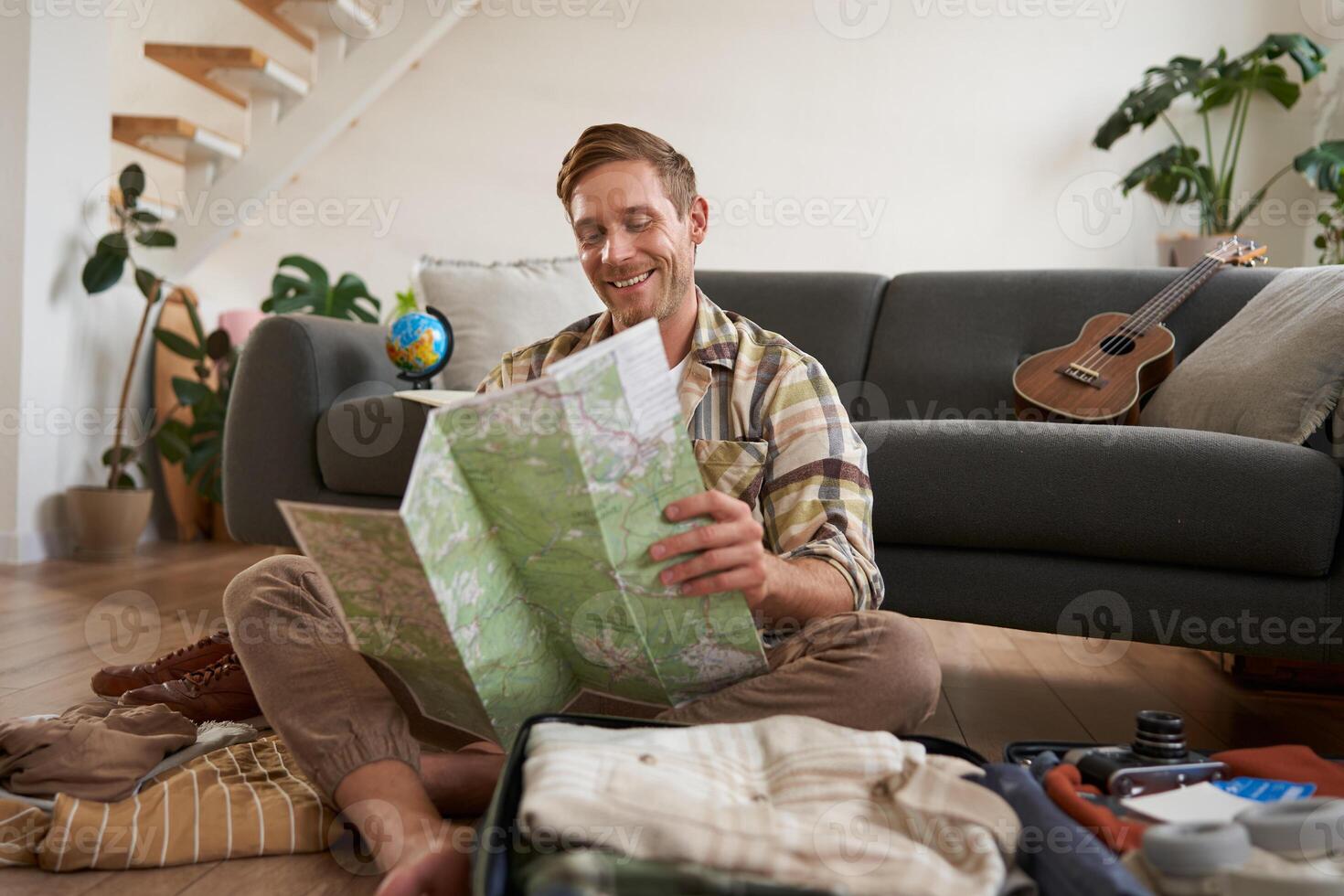 Portrait of handsome young man, traveller with suitcase, looking at paper map, choosing where to go on vacation, going on holiday, choosing route photo