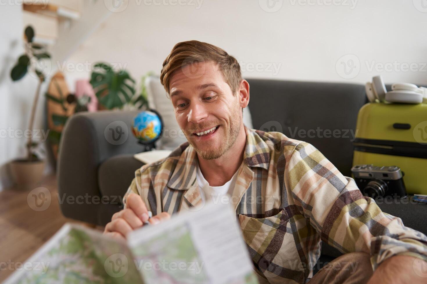 Smiling handsome man with map in hands, packed suitcase, goes on holiday, prepared to go on vacation photo