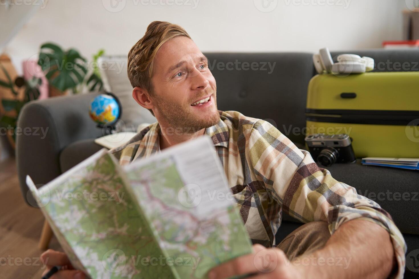 Handsome smiling tourist, man holds map, plans his holiday, going on vacation, looking aside with dreamy, happy face expression photo