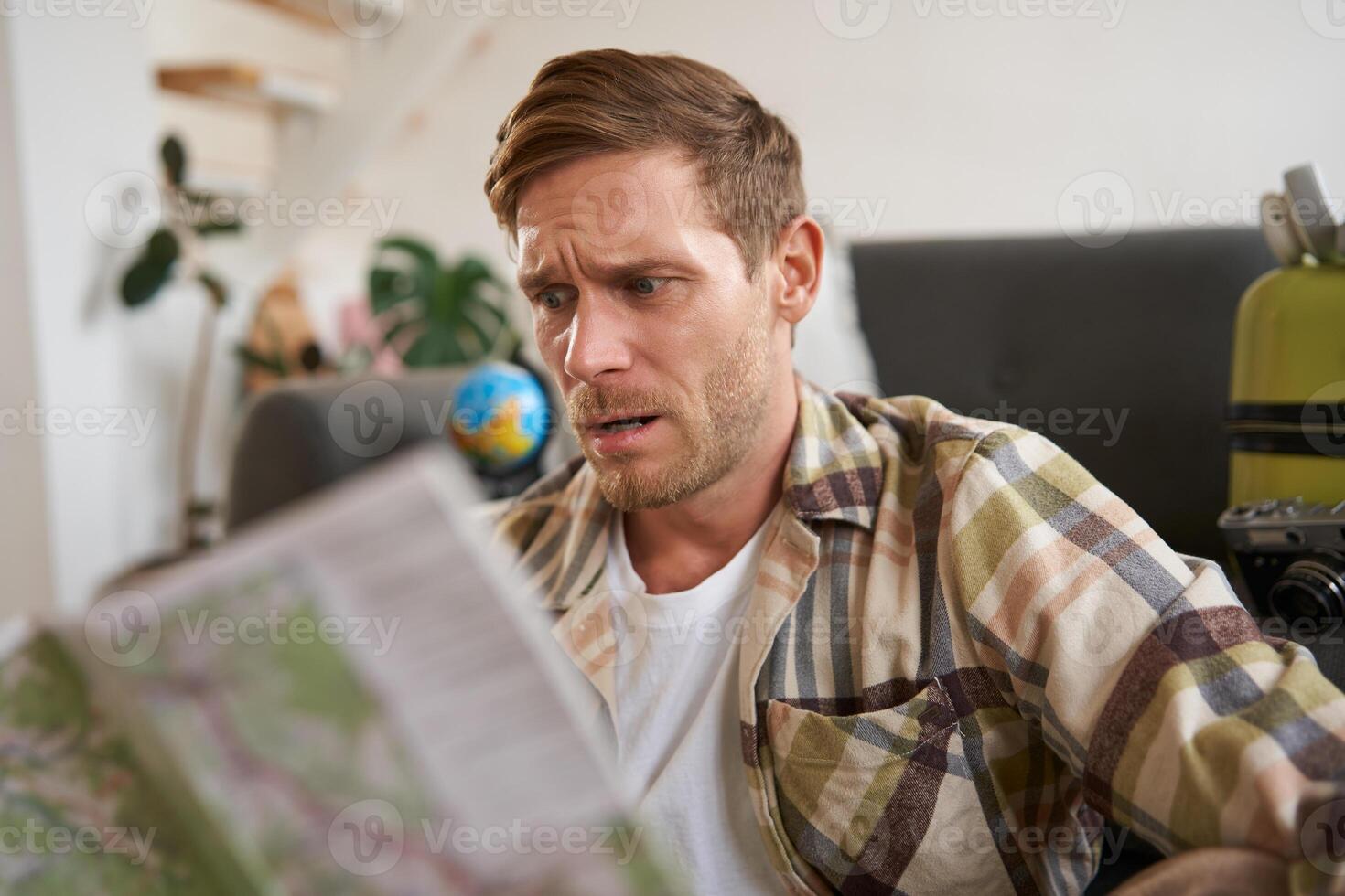 Portrait of confused guy looking at travel map, choosing route, going on holiday, plans to go on vacation photo