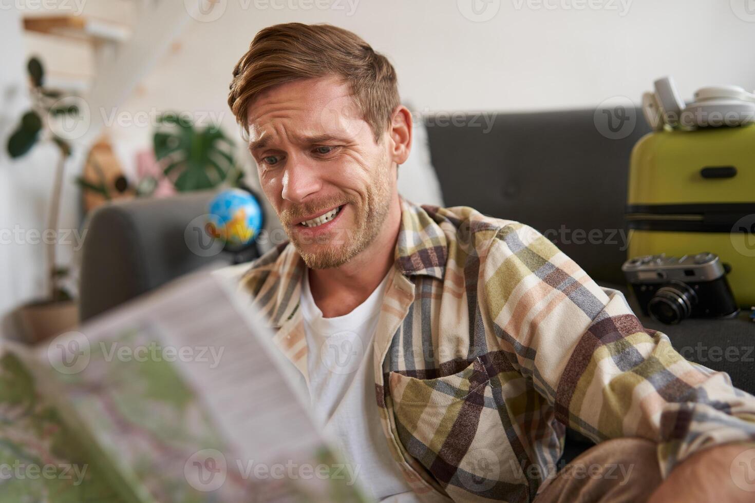 Smiling handsome man with map in hands, packed suitcase, goes on holiday, prepared to go on vacation photo