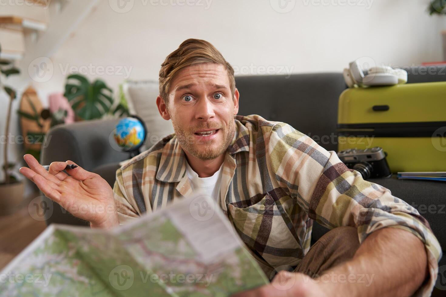 Portrait of man, tourist looking confused at travel map, shrugging, cant decide on route, choosing the road for travelling photo