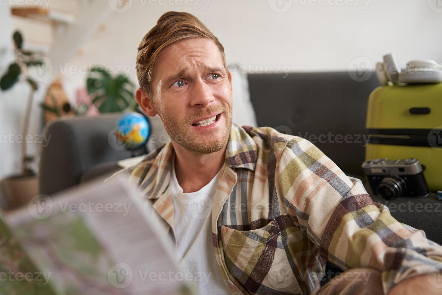 Portrait of man with concerned, stressed face, holding travel map, looking aside, going on vacation photo