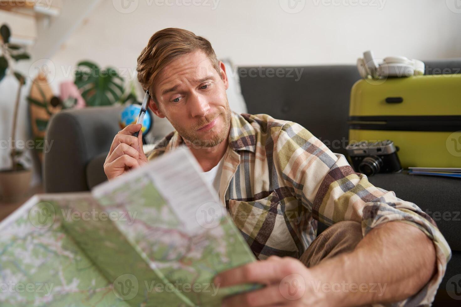 Portrait of man, tourist looking confused at travel map, shrugging, cant decide on route, choosing the road for travelling photo