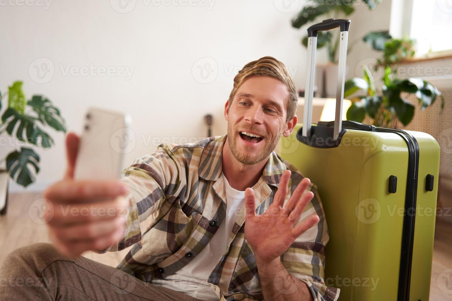 Lifestyle blogger takes photos with his suitcase, shows luggage, goes on holiday, makes selfies on mobile phone