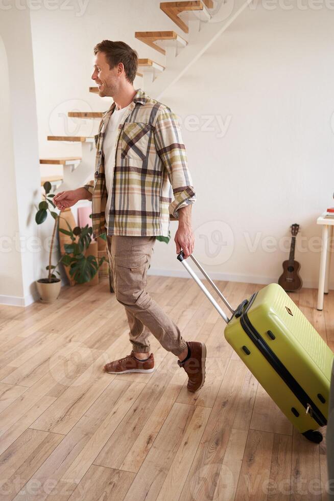 Full length photo of young man with suitcase, going on holiday trip, walking in flat, checking out from rented apartment