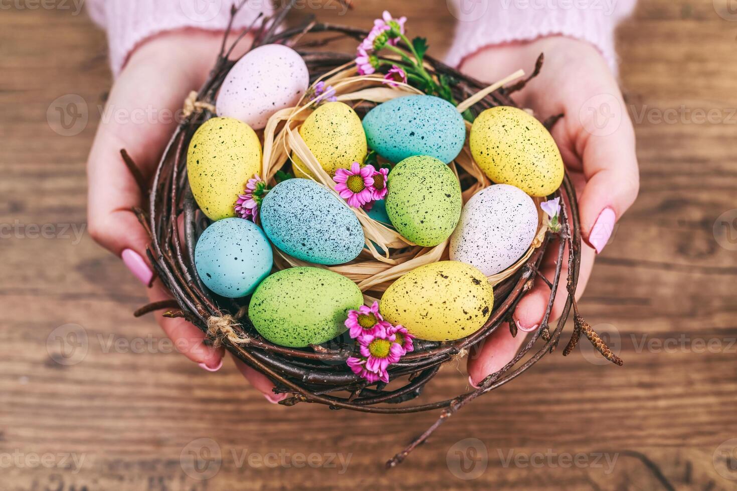 Woman hands holding painted easter egg in a small nest. Toned picture. Top view. Selective focus. photo
