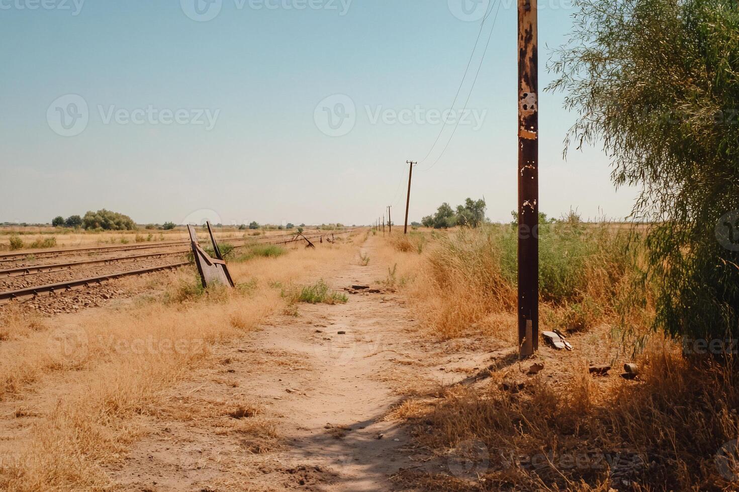 A dusty path alongside railway tracks in a rural landscape. photo