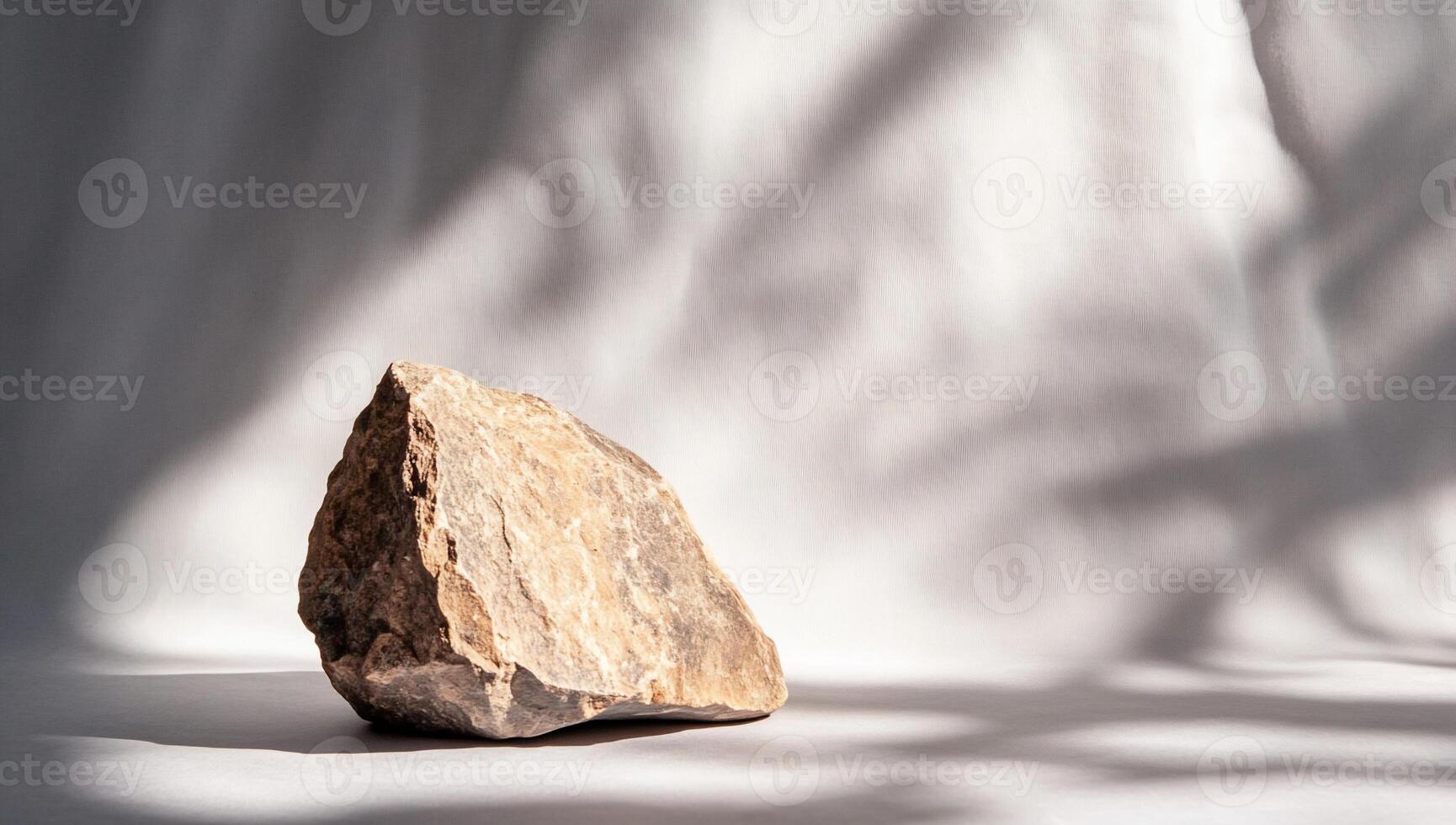 A solitary rock positioned on a soft surface with gentle shadows. photo