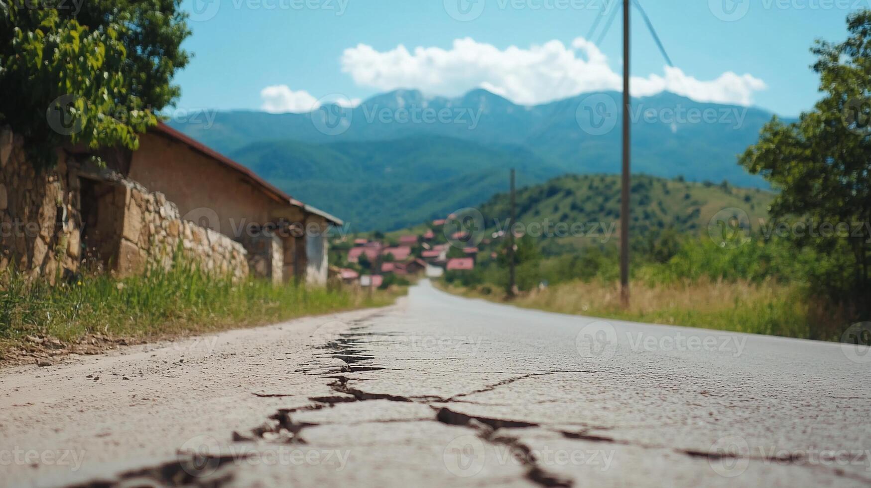 A cracked road leads through a scenic rural landscape with mountains. photo