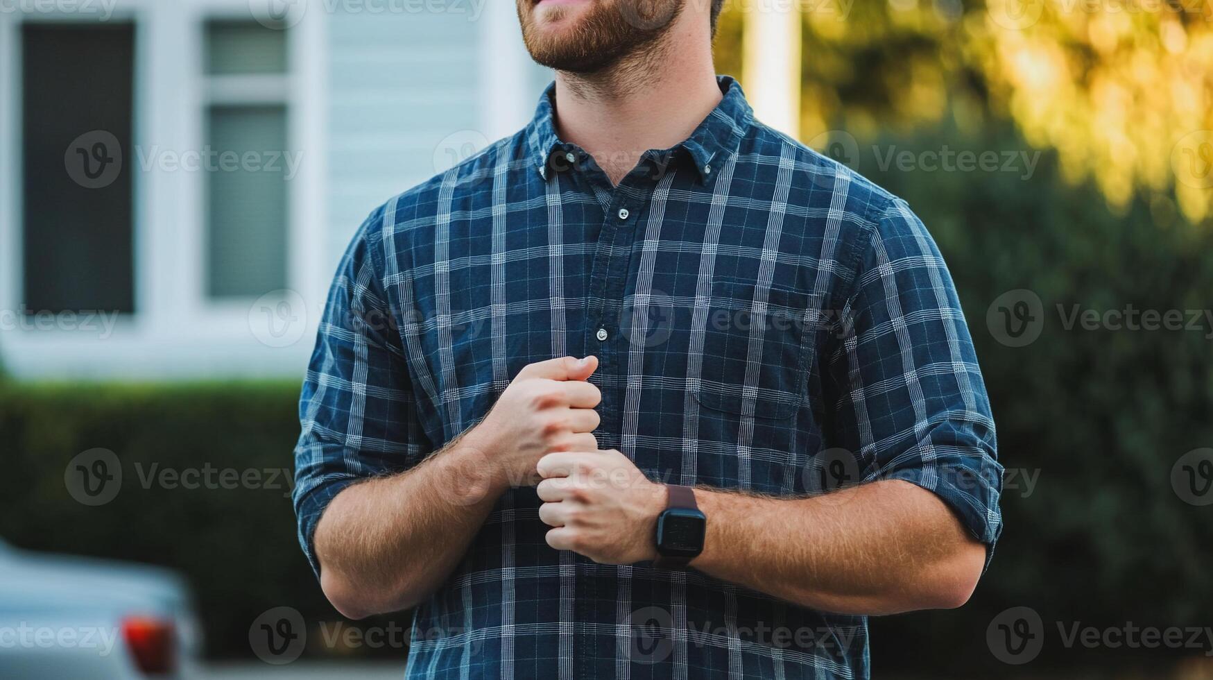 A man in a plaid shirt stands outdoors, looking thoughtful and relaxed. photo