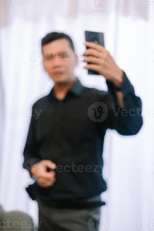 Blurred image depicting a man using his smartphone for selfie indoors photo