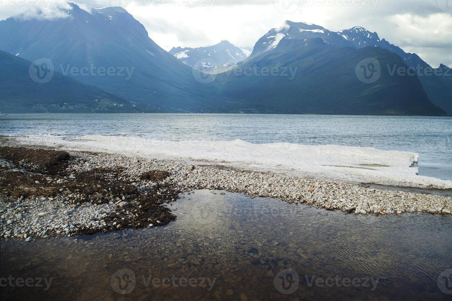 A person standing on a rocky shore with a mountain in the background photo