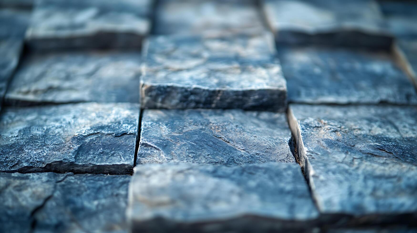 Close-up of a textured wall of stone square tiles. The tiles are different sizes and textures, and they are varying tones of grey and blue. photo
