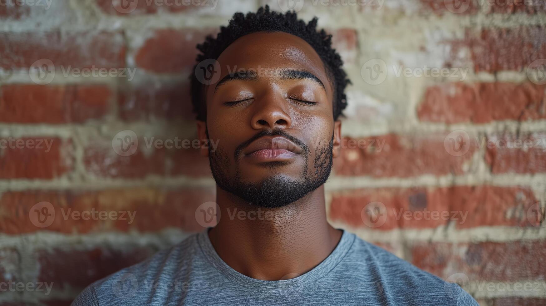 A man with his eyes closed and his head resting against a brick wall photo