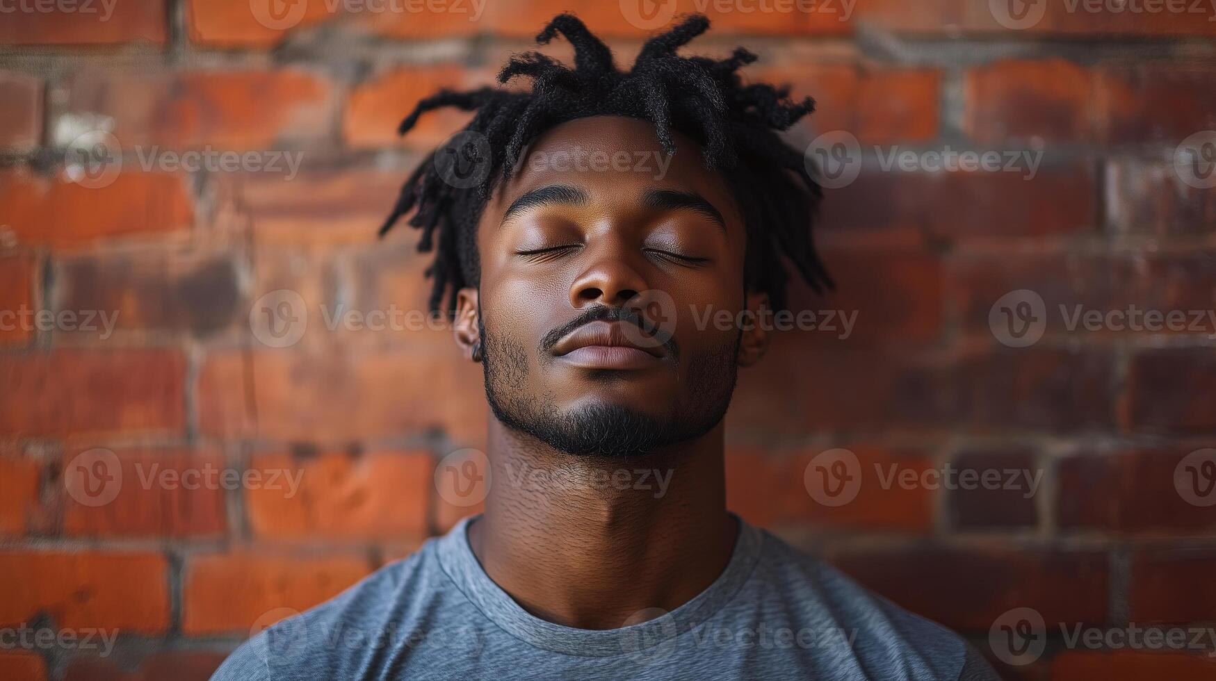 A man with dreadlocks is sleeping against a brick wall photo