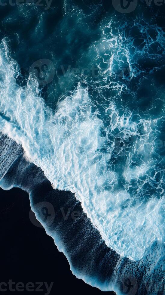Ocean waves crashing on black sand beach creating white foam aerial view photo