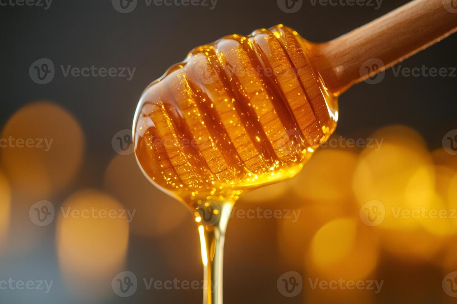 Honey dripping from wooden honey dipper with golden bokeh background .. photo