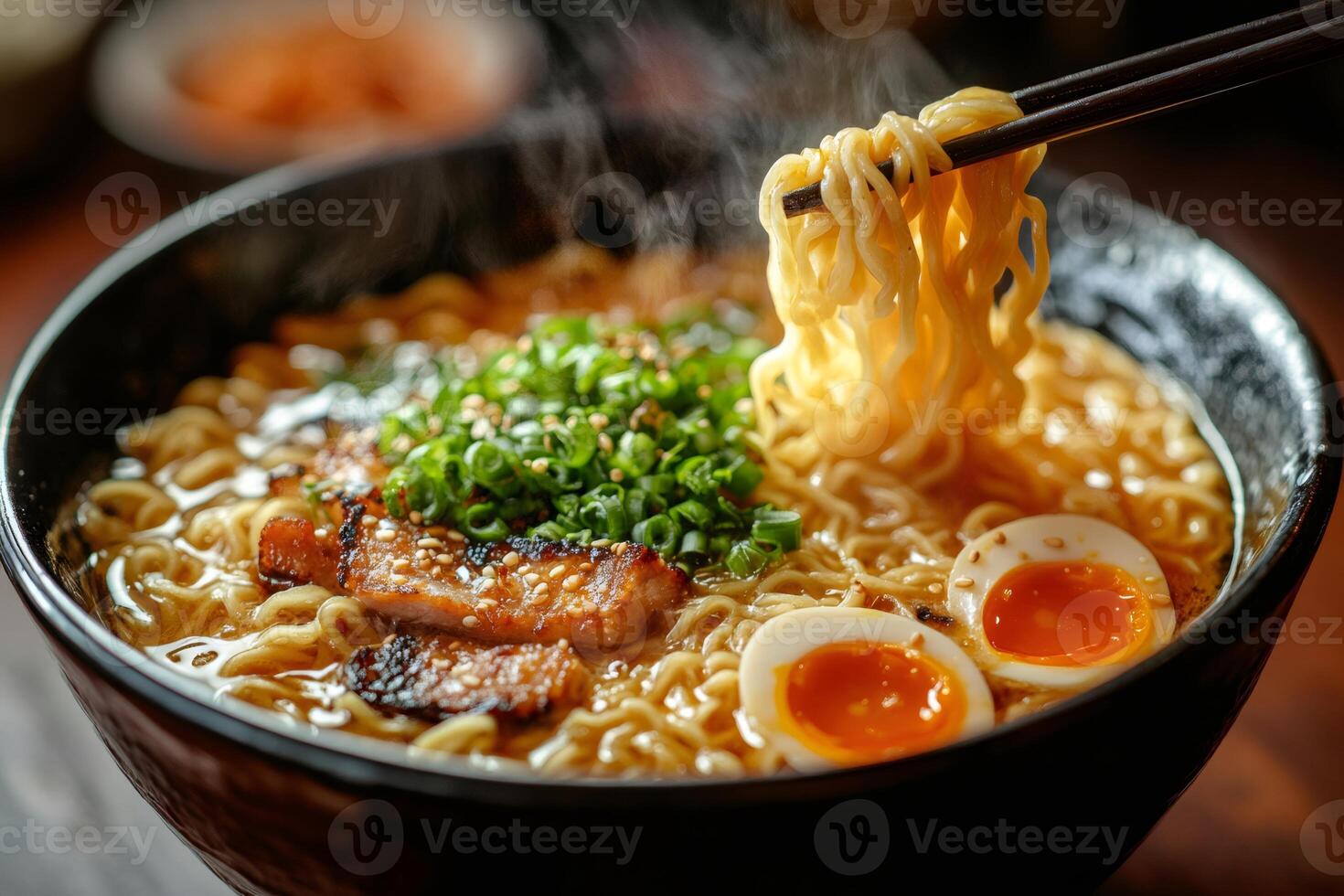Chopsticks lifting noodles from steaming bowl of ramen with pork and egg photo