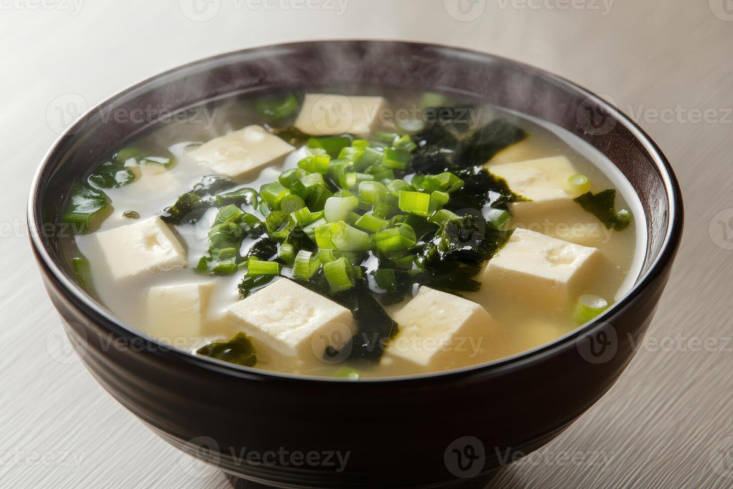 A steaming bowl of miso soup with tofu, seaweed, and green onions photo