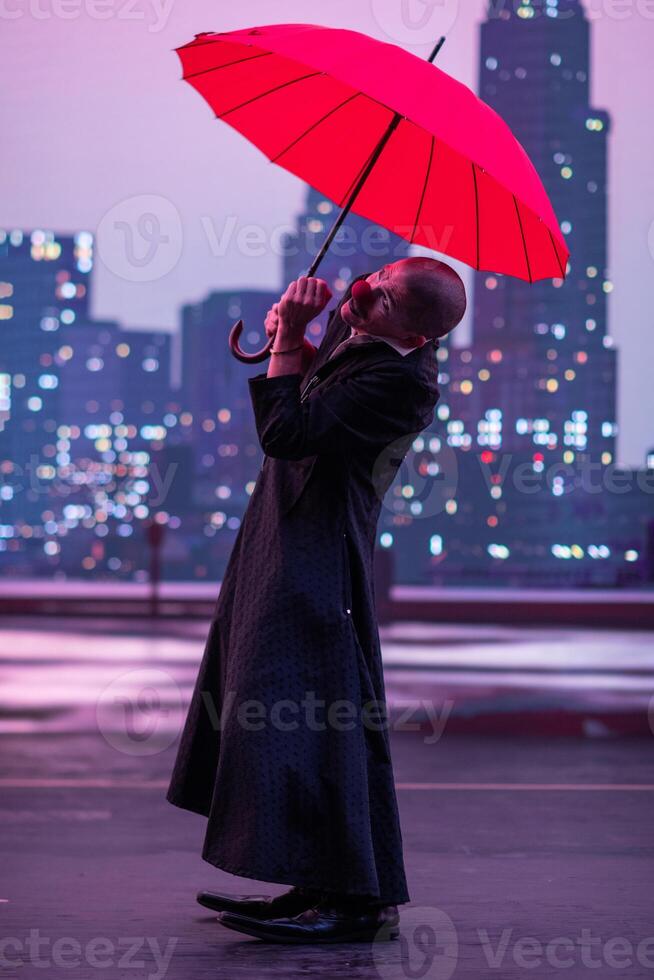 Mysterious Clown Performer with Red Umbrella in Urban Nightscape. photo