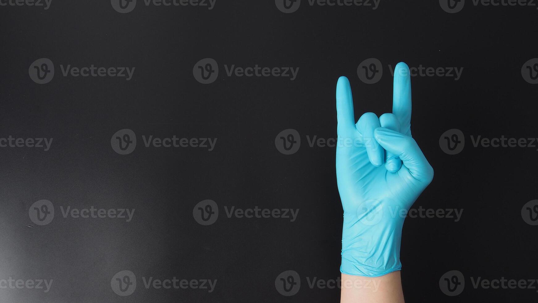 Hand is wear blue glove and doing i love you hand sign on black background. photo