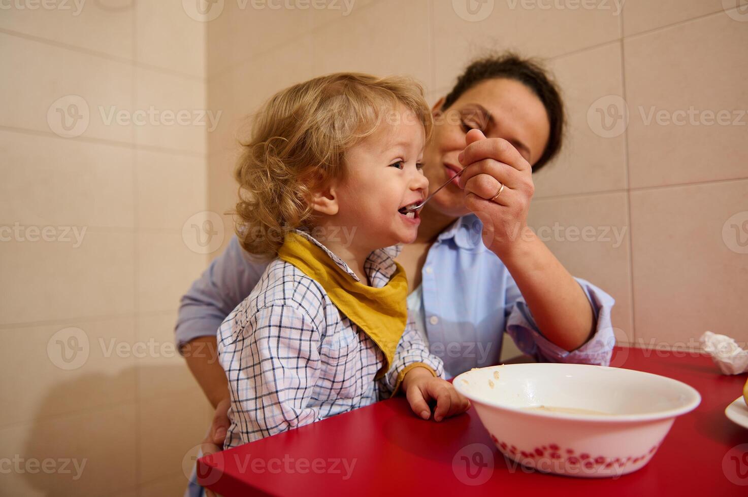 Mother Feeding Her Happy Child a Meal While Sitting Together in a Cozy Kitchen photo