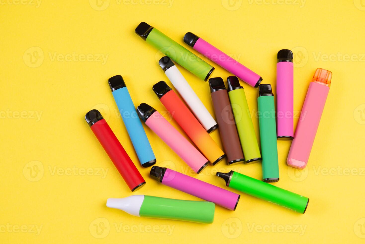 Layout of colorful disposable electronic cigarettes on a yellow background. The concept of modern smoking. photo