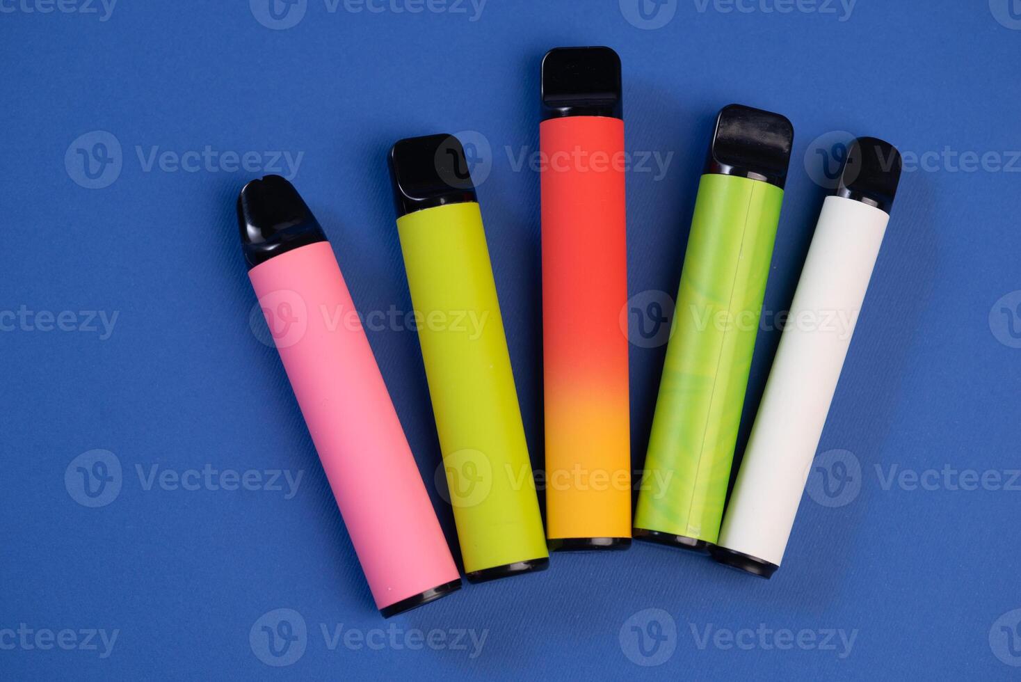Layout of colorful disposable electronic cigarettes on a dark blue background. The concept of modern smoking, Top view photo
