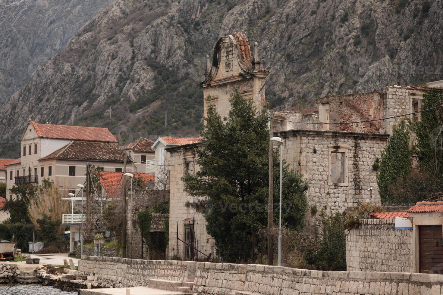 Historical stone buildings by the waterfront in a coastal town with rocky mountains in the background captured on an overcast day in Montenegro photo