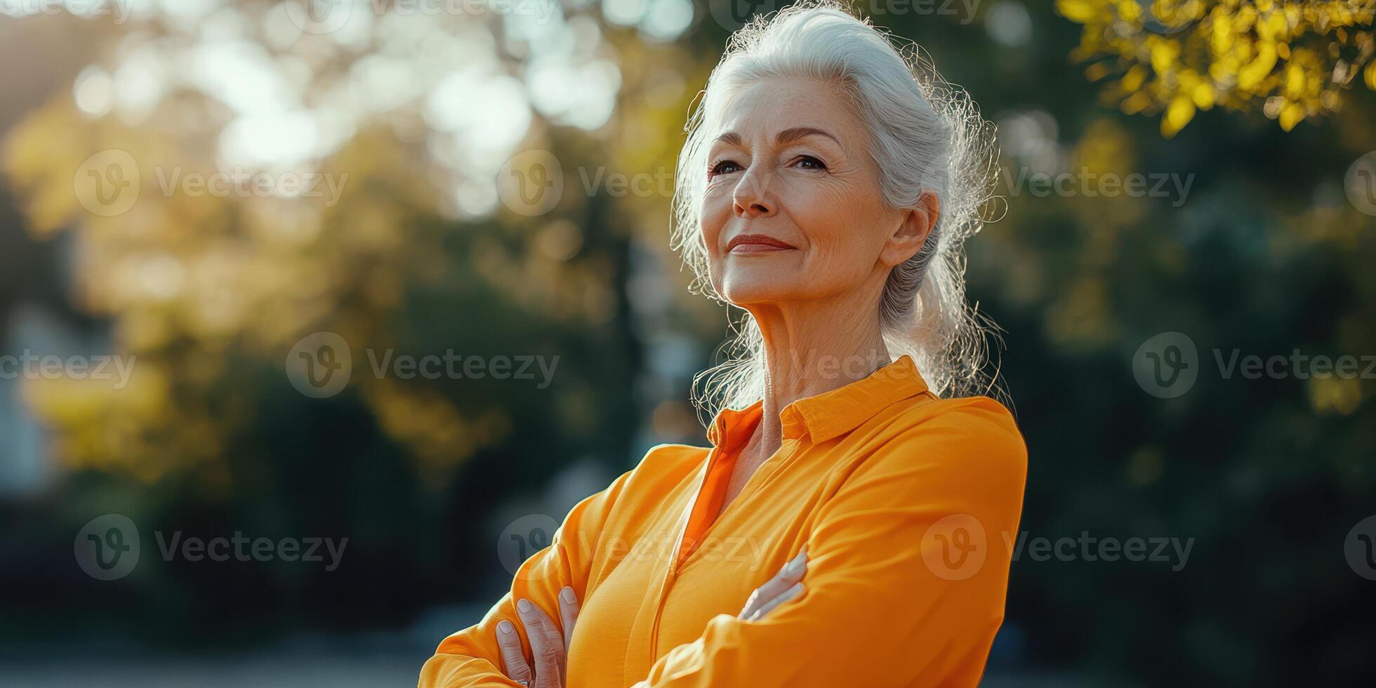 Confident older woman enjoying sunny day in park with arms crossed and serene expression photo