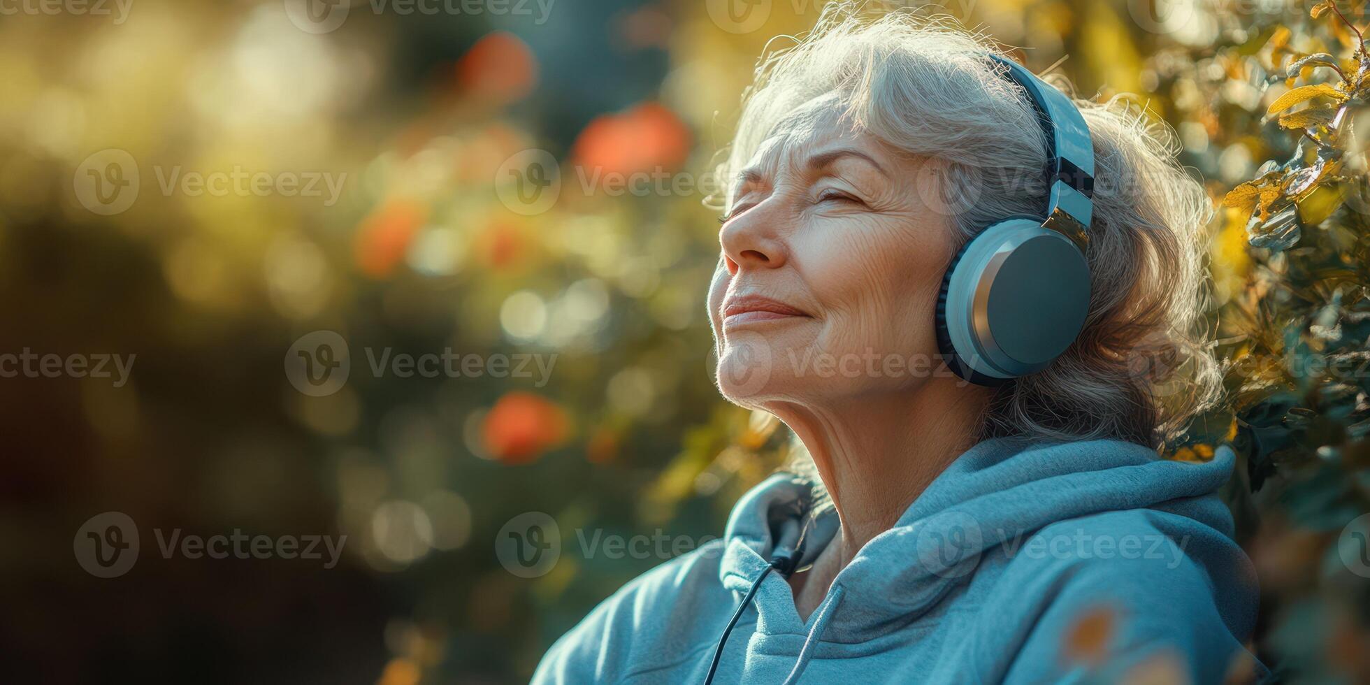 Older woman enjoying music outdoors while relaxing in a sunny garden with blooming flowers all around her photo
