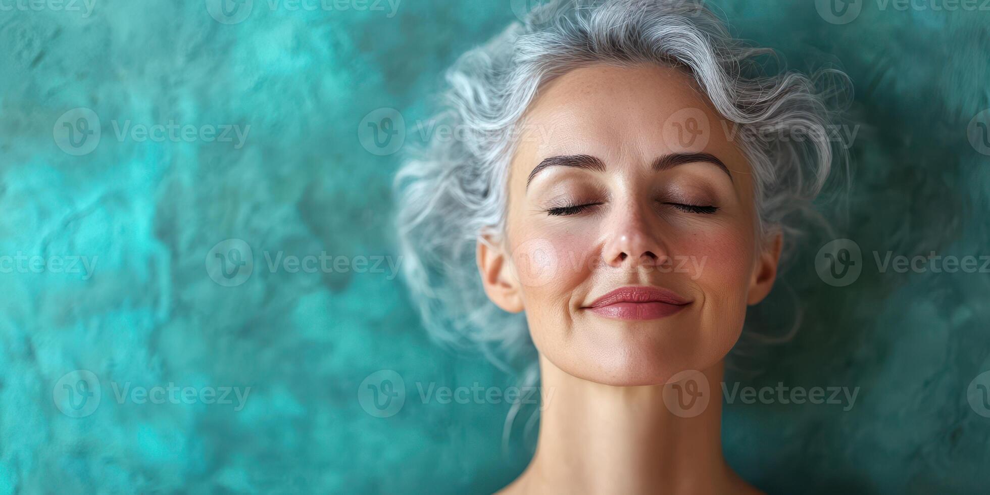Woman with gray hair enjoys a moment of calm against a teal background while practicing mindfulness photo