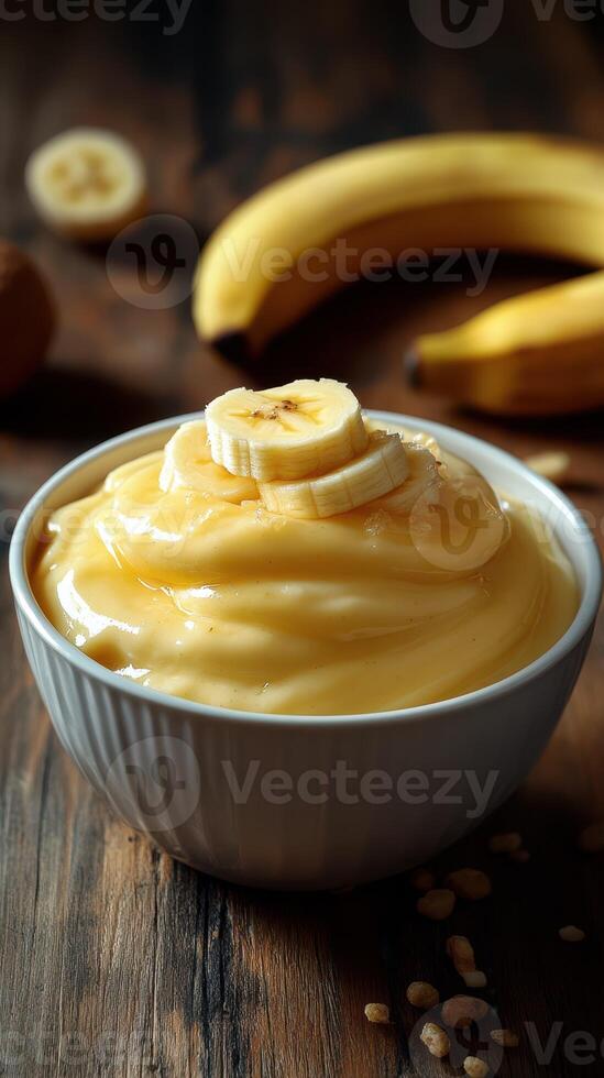 Creamy banana pudding served in a bowl with fresh bananas in the background on a wooden table photo