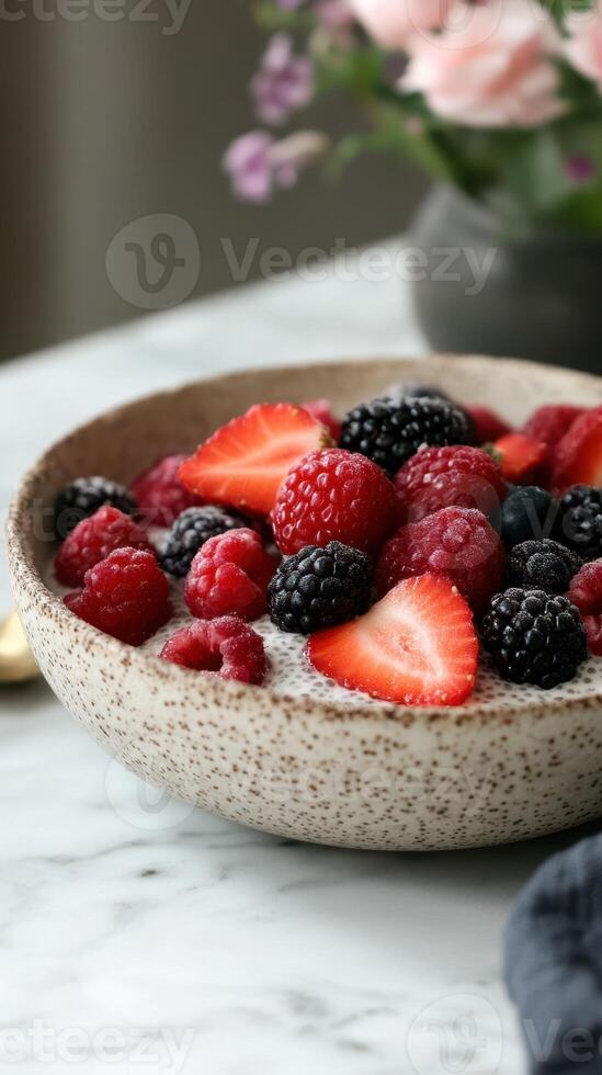 Delicious bowl of fresh berries with texture on marble table with flowers in background photo
