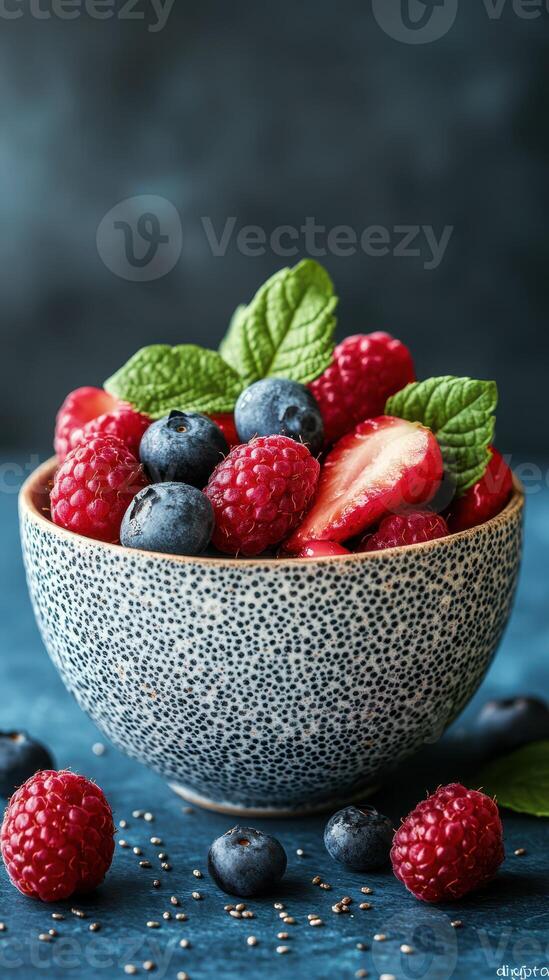 Fresh berries in a textured bowl with mint leaves arranged on a blue surface with chia seeds scattered around photo