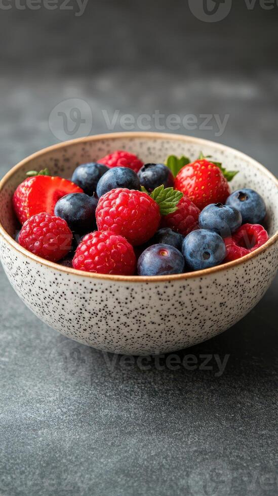 Fresh mixed berries in a speckled bowl resting on a textured surface photo