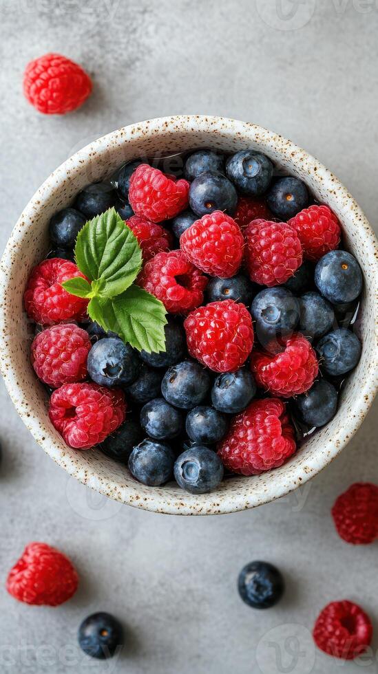Fresh berries in a rustic bowl on a textured surface with green leaves for a healthy snack or dessert option photo