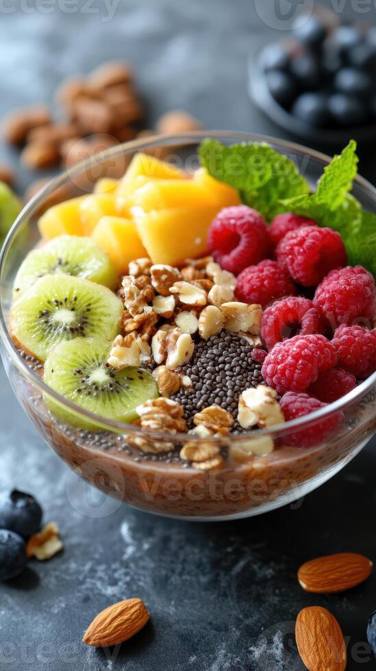 Colorful fruit and grain bowl topped with fresh berries and nuts served in a glass bowl on a dark surface photo
