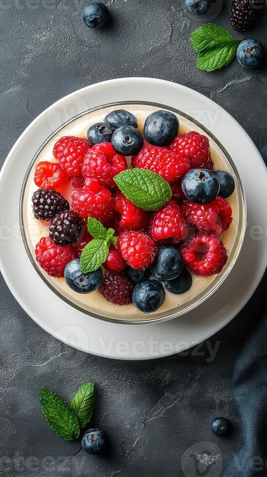 Fresh berry dessert topped with mint leaves in a clear bowl on a dark background photo