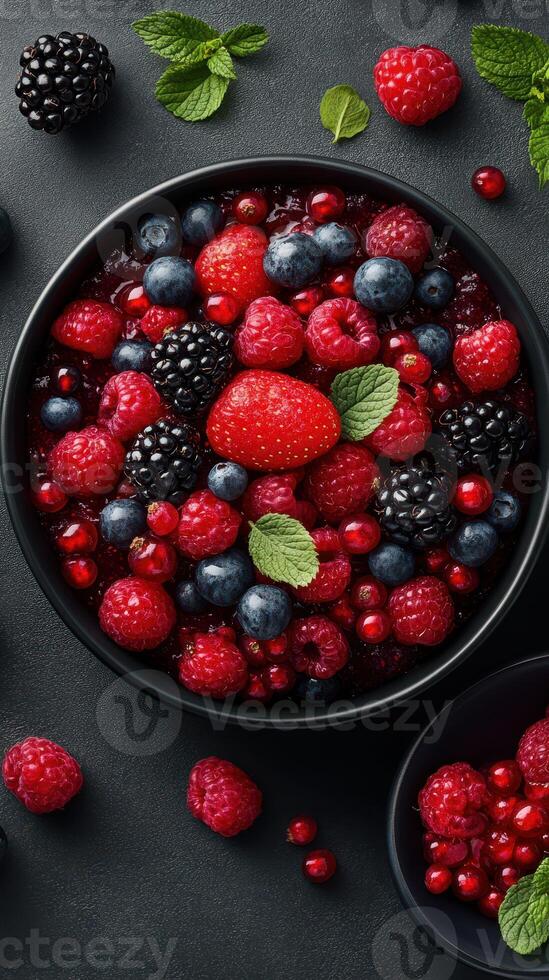 Fresh assortment of mixed berries in a bowl on a dark textured surface with vibrant colors and details photo