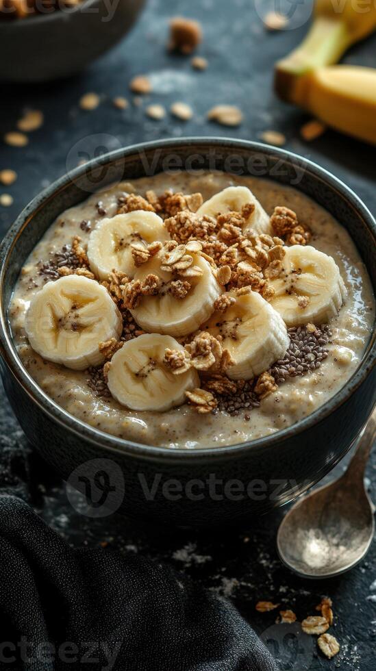 Healthy breakfast bowl with banana slices, granola, and chia seeds topped with oatmeal in a dark setting photo